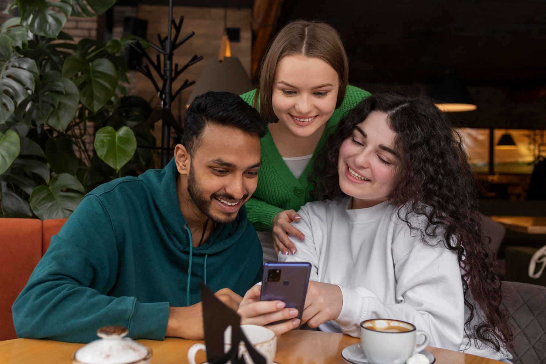 Three friends at a café table smiling at a phone together
